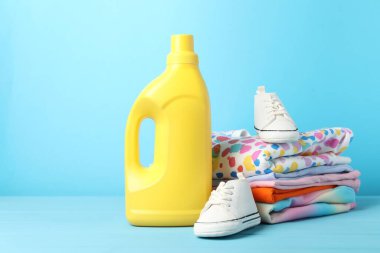 Şişe yumuşatıcı, bebek kıyafetleri ve açık mavi ahşap masa üzerindeki ayakkabılar.