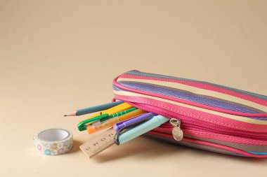 Bej arka planda kalem kutusunda farklı kırtasiye malzemesi, yakın plan