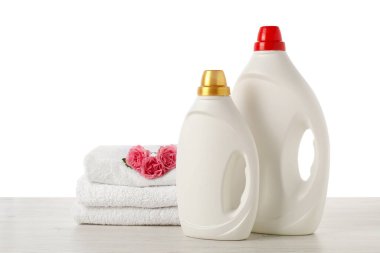 Kumaş yumuşatıcı şişeler, beyaz arka plana karşı ahşap masa üzerine istiflenmiş havlular ve çiçekler.