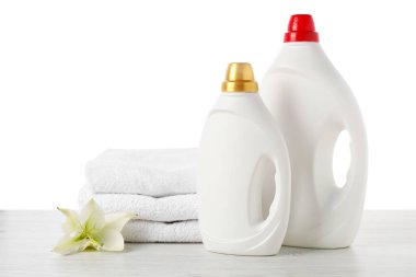 Kumaş yumuşatıcı şişeler, beyaz arka plana karşı ahşap masa üzerine istiflenmiş havlular ve çiçekler.