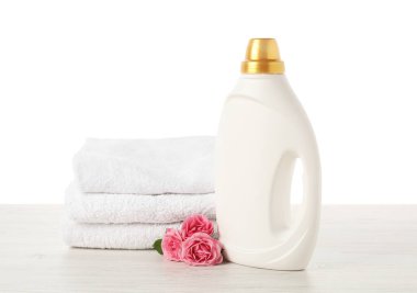 Bir şişe yumuşatıcı, beyaz arka plana karşı ahşap masa üzerine yığılmış havlular ve çiçekler.