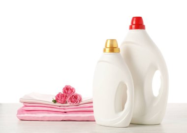 Kumaş yumuşatıcı şişeler, beyaz arka plana karşı ahşap masaya dizilmiş giysiler ve çiçekler.