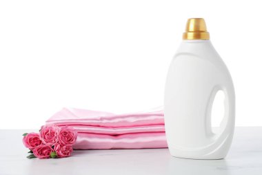 Bir şişe yumuşatıcı, beyaz arkaplan karşısında üst üste yığılmış giysiler ve çiçekler.