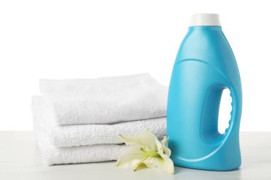 Bir şişe yumuşatıcı, beyaz arkaplana karşı mermer masaya istiflenmiş havlu ve çiçek.