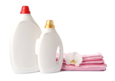 Kumaş yumuşatıcısı şişeleri, üst üste yığılmış giysiler ve beyaz üzerine izole edilmiş çiçekler.
