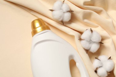 Bir şişe yumuşatıcı ve bej arka planda pamuk çiçekleri.