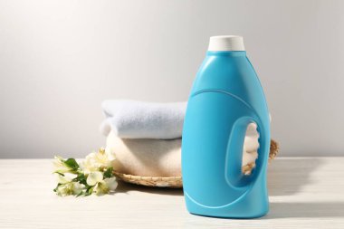 Bir şişe yumuşatıcı, temiz kıyafetler ve beyaz ahşap masa üzerinde zambak çiçekleri.