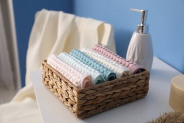 Hasır sepetin içinde temiz waffle havluları banyoda beyaz şifoniyerin üzerinde, yakın plan.