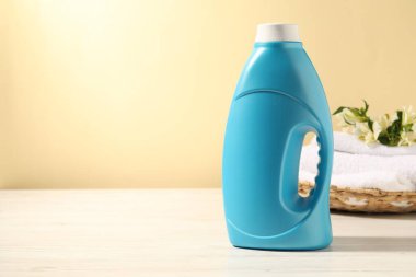 Bir şişe yumuşatıcı, terry havlular ve açık sarı arka planda beyaz ahşap masada zambak çiçekleri. Metin için boşluk