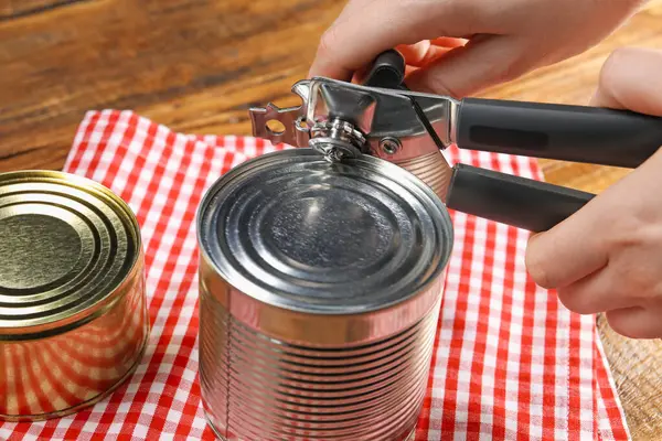 Kadın konserve açacağıyla konserve açıyor. Ahşap masada, yakın plan.