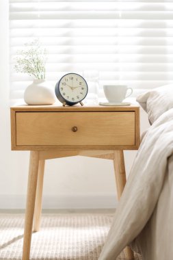 Komodinin yanında çalar saat, vazoda çiçekler, yatağın yanında bardak ve bardak su.