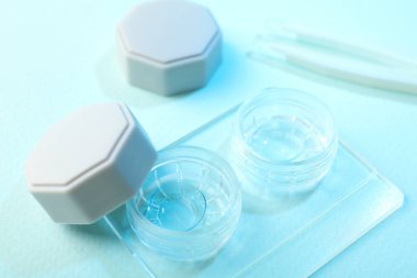 Açık mavi arkaplanda kontak lens ve cımbızlı dosya, yakın plan