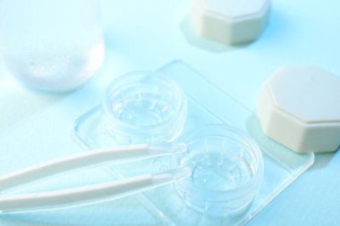 Açık mavi arkaplanda kontak lens ve cımbızlı dosya, yakın plan