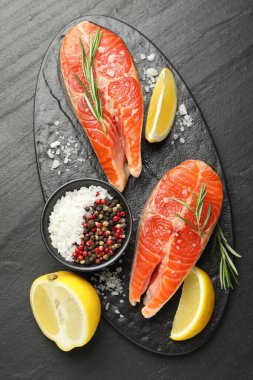 Deniz ürünleri. Siyah desenli masada somon biftekleri, baharatlar ve limon.