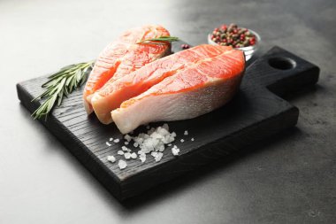 Deniz ürünleri. Çiğ somon bifteği, biberiye ve baharatlar gri masada, yakın plan.