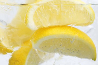 Beyaz arka planda limon dilimleri ve buzla soda tazeleniyor. Yakın plan.