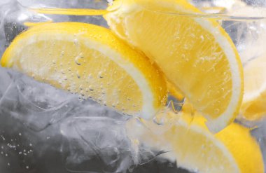 Koyu arkaplanda limon dilimleri ve buzla soda tazeleniyor. Yakın plan.