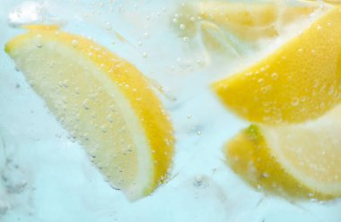 Açık mavi arka planda limon dilimleri ve buzla soda tazeleniyor. Yakın plan.