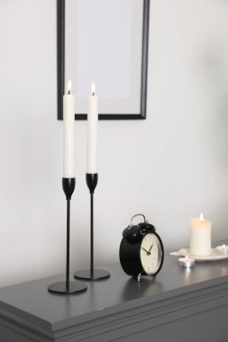 Beyaz duvarın yanındaki şöminenin üzerinde yanan mumlar ve alarm saati olan şık şamdanlar.