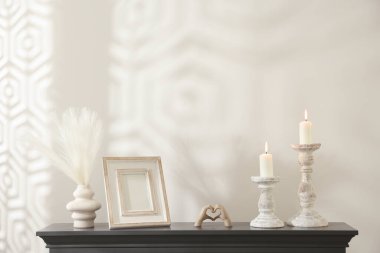 Beyaz duvarın yanındaki şöminede yanan mumlar ve diğer dekorlarla süslü şamdanlar.