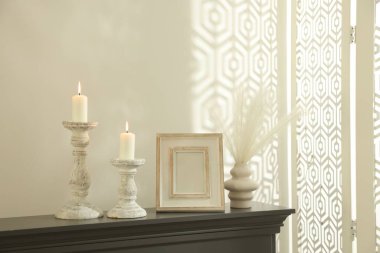 Beyaz duvarın yanındaki şöminede yanan mumlar ve diğer dekorlarla süslü şamdanlar.