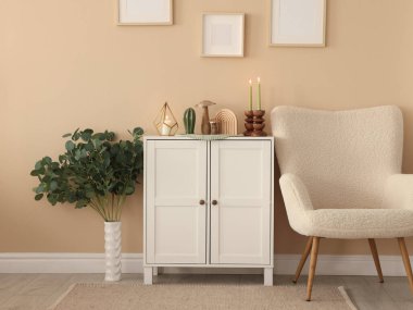 Havalı şamdanlar, yanan mumlar ve kapalı alandaki bej duvarın yanındaki dolaptaki diğer dekorlar.