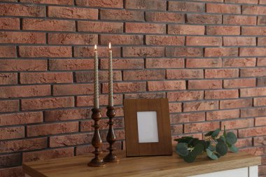 Mum ve tuğla duvarın yanındaki masada yanan mumlar.