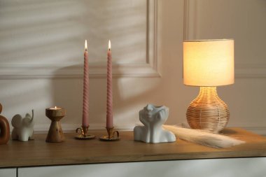 Beyaz duvarın yanındaki çekmecelerin üzerinde yanan mumlar olan şamdanlar.