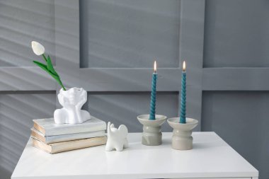 Mum ve yanan mumlar gri duvarın yanındaki masada.