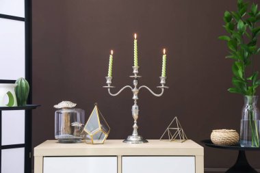 Kahverengi duvarın yanındaki dolapta yanan mumlar ve dekorlar olan zarif bir şamdan.