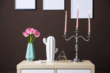 Kahverengi duvarın yanındaki dolapta yanan mumlar ve dekorlar olan zarif bir şamdan.