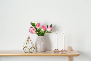 Mumları yanan zarif tutucular, vazoda laleler ve beyaz duvarın yanındaki ahşap masa üzerindeki diğer dekorlar.