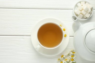 Fincanda nefis papatya çayı, taze çiçekler, şeker küpleri ve çaydanlık beyaz ahşap masa, düz yatak. Metin için boşluk