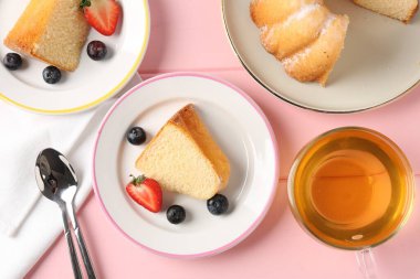 Lezzetli kek parçaları, böğürtlenli ve pembe ahşap masada çay, düz uzanmış.