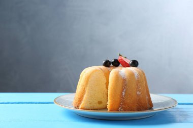 Açık mavi ahşap masa üzerinde pudra şekeri ve böğürtlenli Lezzetli kek, yakın plan. Metin için boşluk