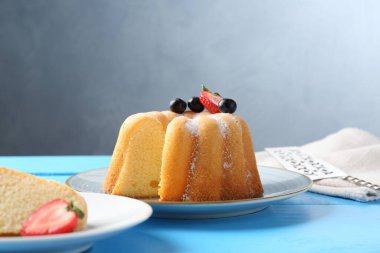 Açık mavi ahşap masada pudra şekerli ve dutlu Lezzetli kek, yakın plan.