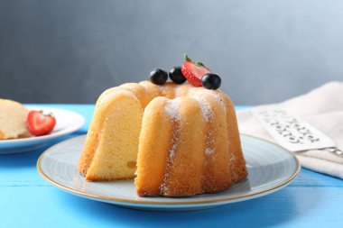 Açık mavi ahşap masada pudra şekerli ve dutlu Lezzetli kek, yakın plan.