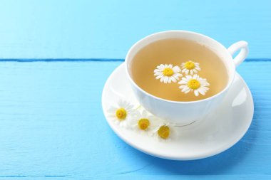 Fincanda nefis papatya çayı ve açık mavi ahşap masada taze çiçekler, yakın plan. Metin için boşluk