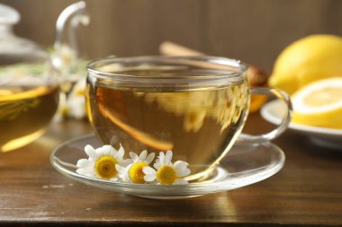 Cam bardakta nefis papatya çayı, taze çiçekler ve ahşap masada limon, yakın plan.