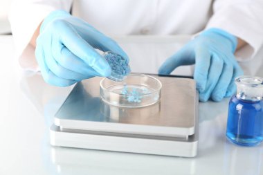 Bilim adamı beyaz ayna masasındaki terazide numune tartıyor, yakın plan.