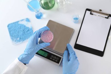 Beyaz masada Petri kabı ve ölçekleriyle çalışan bilim adamı.