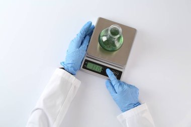 Bilim adamı beyaz masadaki terazide numune tartıyor.