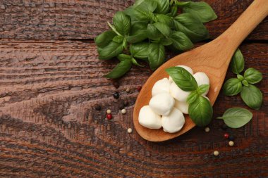 Tasty mozzarella cheese balls in spoon, peppercorns and basil on wooden table, flat lay. Space for text