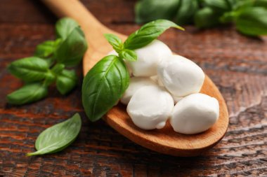 Lezzetli mozzarella peyniri topları kaşıkta fesleğen ve ahşap masada, yakın plan.