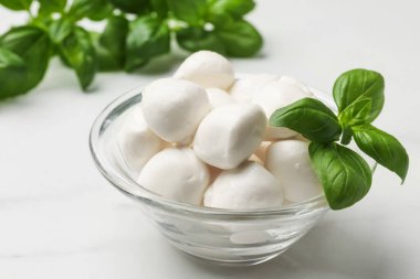 Lezzetli mozzarella peynir topları kasede ve fesleğen beyaz mermer masada, yakın plan.