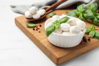Lezzetli mozzarella peynir topları kasede, kaşıkta, fesleğende ve biberlikte beyaz mermer masada, yakın plan