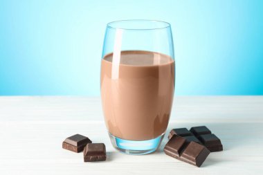 Bardakta çikolatalı süt ve beyaz ahşap masada açık mavi arka planda parçalar, yakın plan.