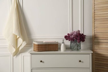 Temiz waffle havluları ve vazo dolusu leylak çiçekleri banyodaki beyaz şifoniyerde.