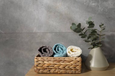 Gri duvarın yanındaki ahşap şifoniyerde dalları olan waffle havluları ve vazolar.