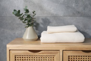 Gri duvarın yanındaki ahşap şifoniyerde dalları olan gözleme havluları ve vazolar.